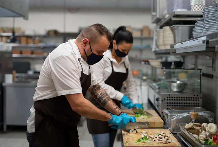 A chef and assistant using two knives to cut vegetables in a restaurant kitchen.