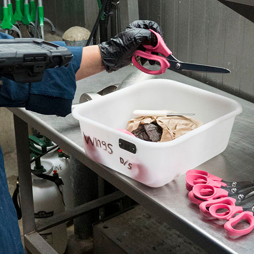A worker checks out a pair of scissors using a scanner that is part of an asset tracking and management system for poultry processing.