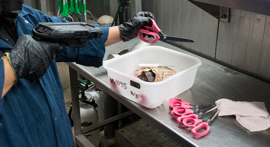 A worker checks out a pair of scissors using a scanner that is part of an asset tracking and management system for poultry processing.
